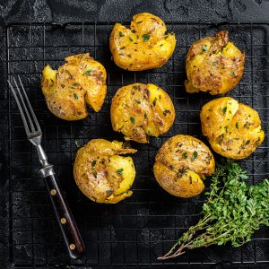 Crushed, smashed potatoes baked with rosemary and thyme. Black background. Top view