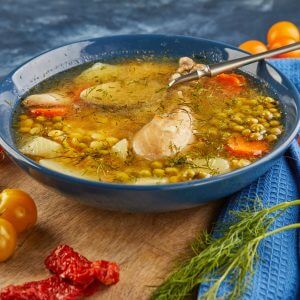 Pea soup with chicken, carrots, tomatoes and herbs in a deep plate on wooden board